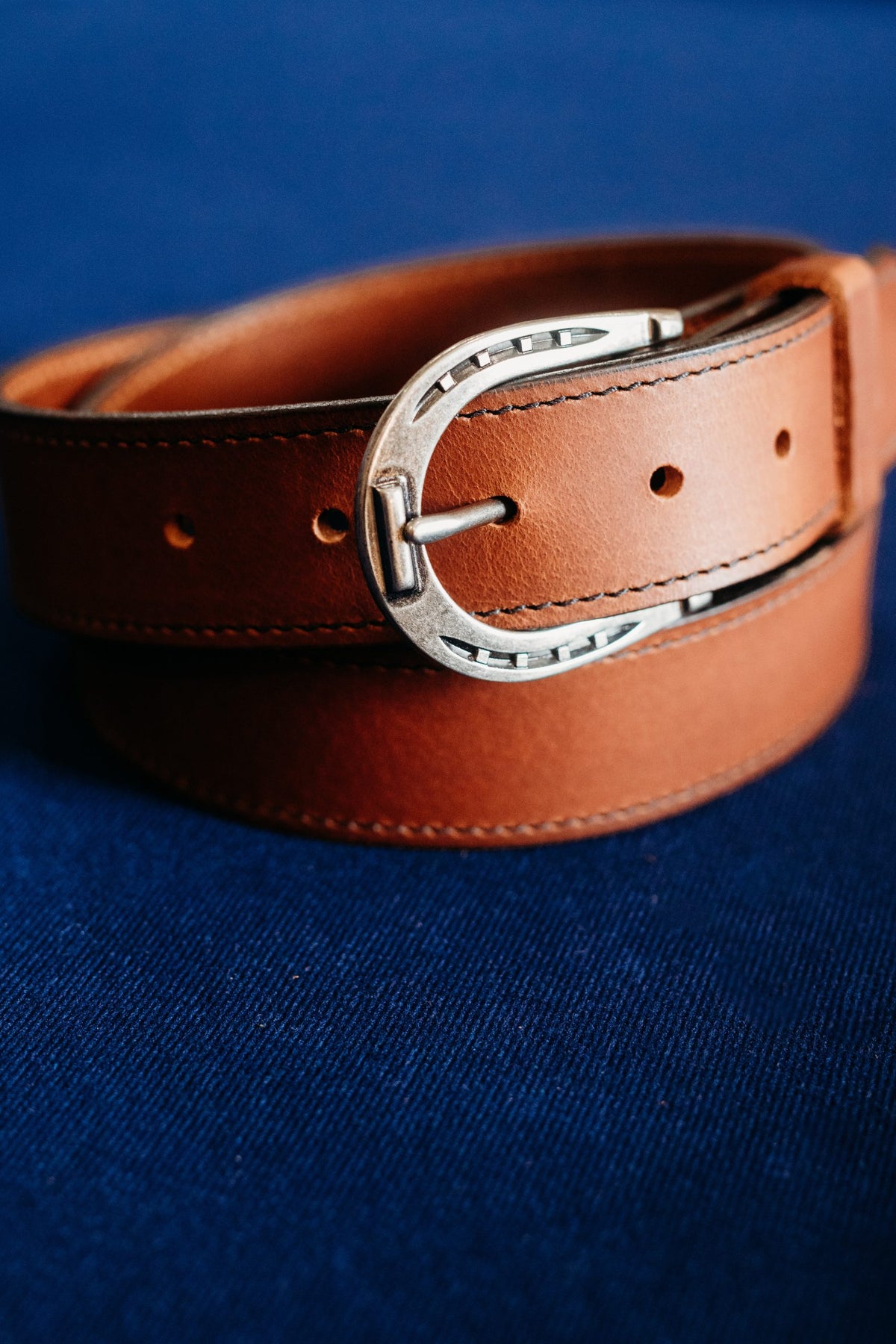 The Shoe full grain leather belt, horseshoe buckle close-up in golden brown